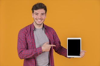 Smiling portrait young man showing something digital tablet against orange background