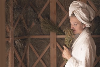 Young woman smelling herb flowers standing sauna