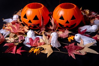 Detail of Halloween pumpkins over red autumn leaves and ghosts on a black background