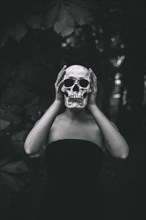Woman holding human skull forest