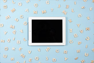 Digital tablet with black screen display surrounded with wooden letters blue background