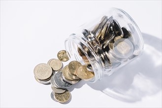 Spilled out coins from glass container white background