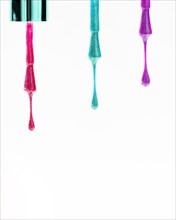 Row colored nail polish dripping from brush white surface