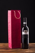 Wine bottle red paper bag wooden table against black backdrop