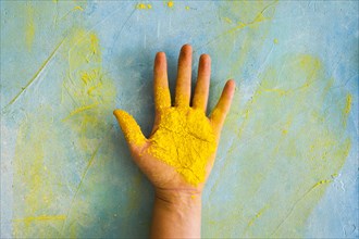 Yellow powder person s palm against painted messy wall with color
