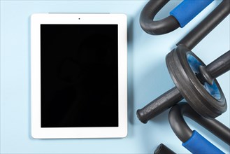 Digital tablet with black display gym equipments blue backdrop