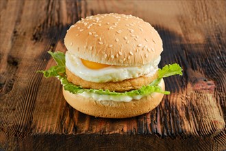 Chicken burger with fried egg and fresh iceberg lettuce salad on wooden board