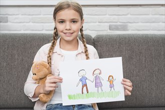 Portrait smiling girl sitting sofa showing her family drawing paper