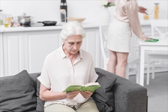 Senior woman sitting sofa reading book home