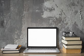 Stacked books spectacles laptop with blank white screen wooden surface