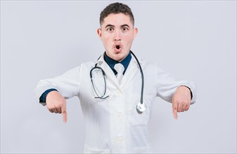 Surprised young doctor pointing down. Amazed male doctor pointing a promo down