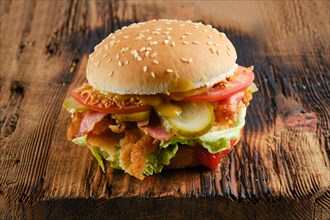 Kentucky chicken burger with pickled cucumber and fresh tomato on wooden background