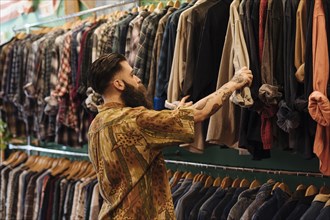 Young man looking shirt hanging rail inside clothing shop
