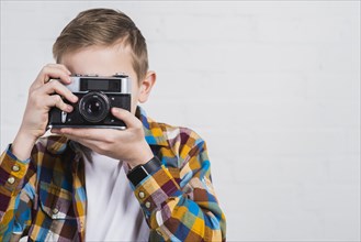Boy taking picture with vintage camera against white background
