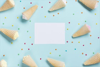 Overhead view waffle cones sprinkles surrounded near white blank paper blue backdrop