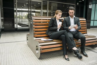 Businesspeople sitting bench looking mobile phone