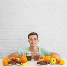 Happy young man holding smoothies with colorful fresh organic fruits desk