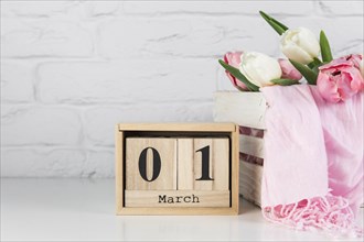 Wooden calendar with 1st march near wooden crate with tulips scarf white desk