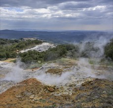 Steam rises above the colourful rubble deposits of the Biancane Geothermal Park and the town in the background