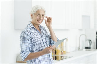 Portrait smiling senior woman holding digital tablet standing kitchen