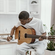Front view male musician home playing guitar writing lyrics
