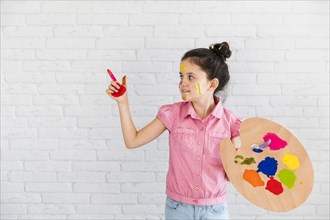 Little girl holding palette showing something with painted red finger