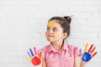 Portrait girl standing against white wall showing colorful painted hands looking away