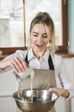 Happy young woman pouring fresh milk mixing bowl
