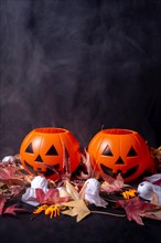 Halloween pumpkins over red autumn leaves and ghosts with smoke on a black background