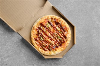 Top view of barbecue pizza with bacon and spring onion in cardboard box