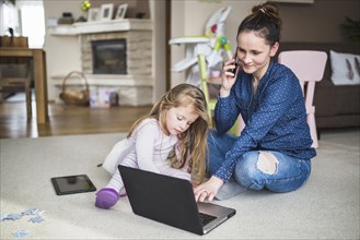 Woman sitting with her daughter talking cellphone while using laptop