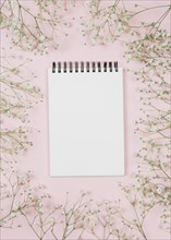 Blank spiral notepad surrounded with gypsophila flowers against pink background