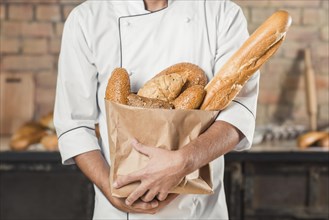 Mid section male baker holding different type breads paper bag