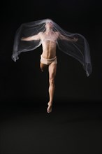 Naked gymnast jumping with transparent cloth