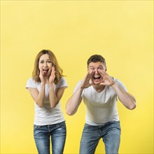 Young couple yelling loudly against yellow background