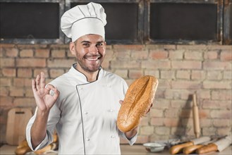 Smiling male baker holding loaf showing ok hand sign gesture