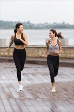 Front view female friends having fun while jogging together outdoors