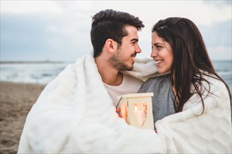 Couple looking each other sand with candle blanket