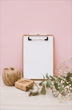 White paper clipboard with spool gift box baby s breath flowers wooden desk against pink background