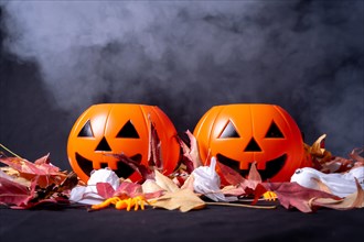 Detail of Halloween pumpkins over red autumn leaves and ghosts with smoke on a black background