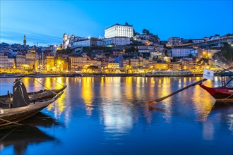 View over the traditional Rabelo boats on the Douro riverbank in Vila Nova de Gaia towards the old town of Porto at dusk