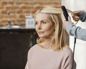 Mature woman getting her hair straightened by hairdresser home