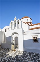 Young man with cat in front of archway with bells of Agios Antonios chapel and Greek Orthodox church Metamorfosi Sotiros
