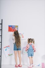 Little girls hanging drawings white wall