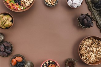 Metallic earthen bowl dried fruits dates lukum nuts baklava arranged circular shapeover brown background