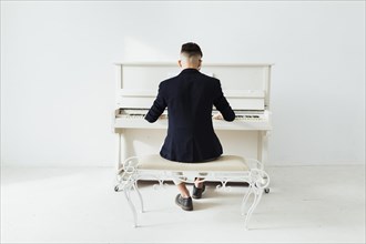 Rear view man playing piano sitting against white wall