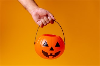 Hand holding an orange Halloween pumpkin on a background of yellow