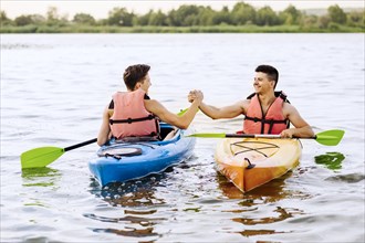 Two male friends shaking each other s hand while kayaking lake