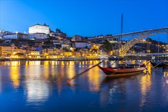 View over the traditional Rabelo boats on the Douro riverbank in Vila Nova de Gaia towards the old town of Porto and the Ponte Dom Luis I bridge at dusk