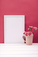 Carnation flower vase with empty frame white wooden table